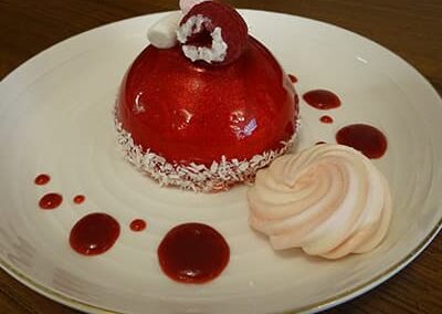 Gateau, glaçage rouge avec une framboise au dessus sur une assiette blanche du restaurant "Les Délices du Cotentin" à Sainte mère église.